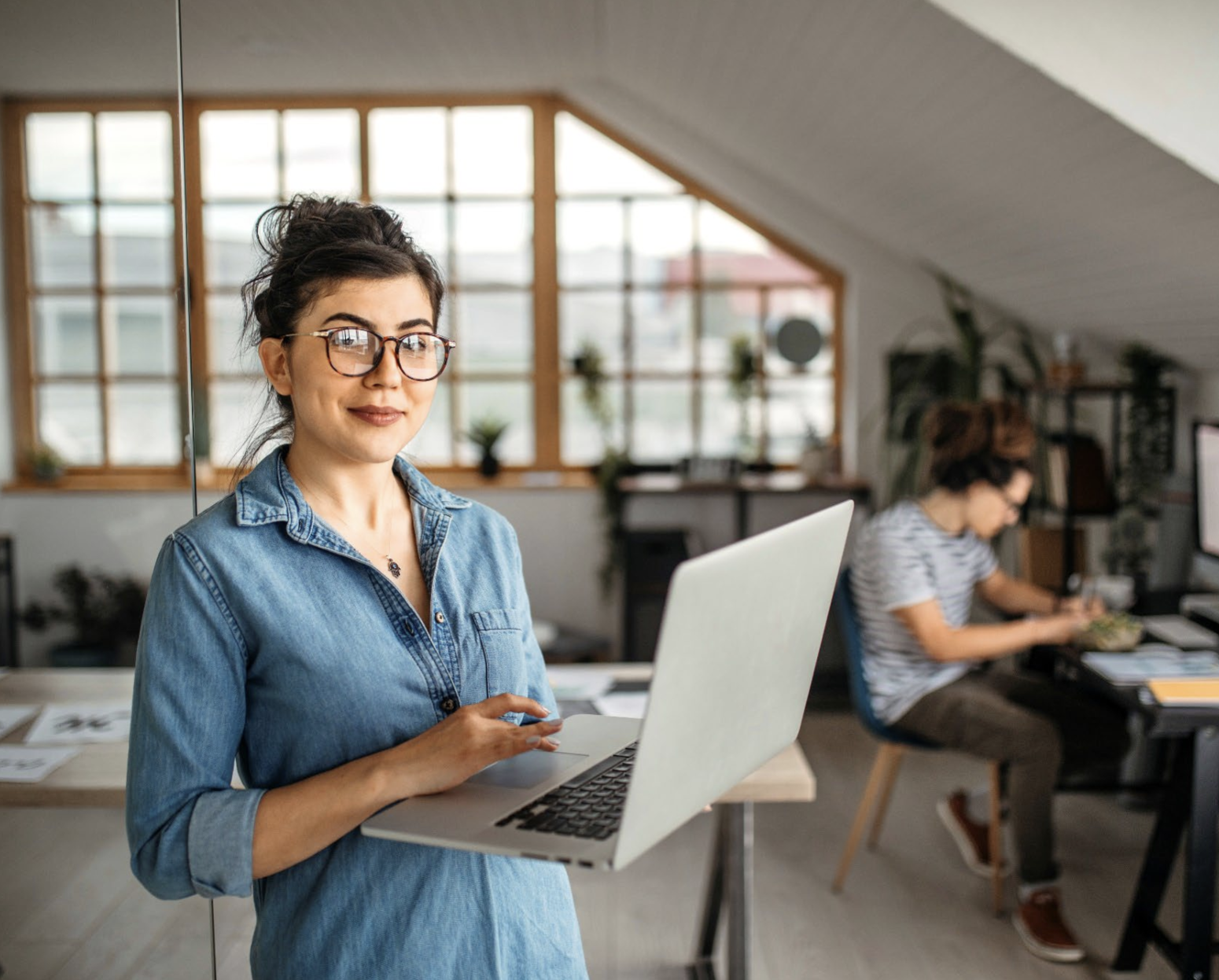 A woman standing holding a laptop in an office